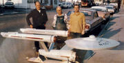 Three persons standing behind the model Enterprise on a streetside