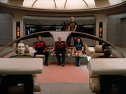 The main cast standing around the bridge of the Enterprise, with two women wearing skirts