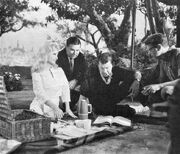 Several persons seated and squatting around the picnic scene