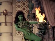 A green woman dances near flames