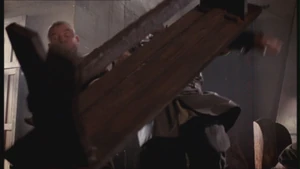 Merlin strikes two thugs with a flying bench.