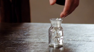 Arthur reaches for glass vial with the tainted water and flower in it