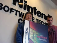 Masamichi Abe y Richard Vorodi sosteniendo una réplica de la carátula de Metroid Prime Hunters: First Hunt.