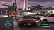 A Nissan 240SX races by a Car Wash-like building in the background. Several traffic vehicles can be seen in the photo as well.