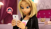Zoé przy łóżku w swoim pokoju trzyma telefon, z którego widać ikonkę z podobizną Marinette.