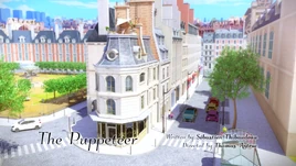 Karta tytułowa odcinka „Lalkarka” z jego tytułem po angielsku, informacją o scenarzyście i reżyserze; tłem jest widok na piekarnię Tom & Sabine od góry