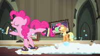 Applejack is putting up a painting of apples while Pinkie Pie scrubs the floor in a skating style.