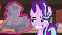 Starlight grinning disinterestedly at pony statuette S7E24