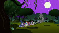 Several young fillies and colts walk to a Nightmare Moon statue.