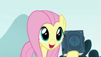 Fluttershy holding the EEA guidebook S8E2