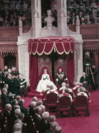 Queen Elizabeth II and Prince Philip sit on thrones before a full Parliament
