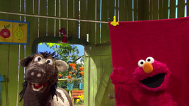 Elmo camouflaging in front of a red towel on Sesamstrasse Folge 2796