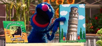 Grover reading about the Leaning Tower of Pisa in The Magical Wand Chase.