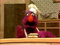 Telly Monster wears a fake mustache and goatee as a chef in a "Cooking with Telly" sketch.
