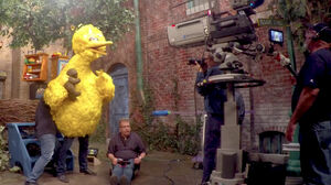 A second puppeteer, concealed behind the puppet, helps Big Bird hold Radar during filming of a Sesame Street scene.