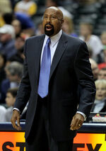 A man, wearing a brown suit and white shirt, is shouting while standing on a basketball court, surrounded by several other people.