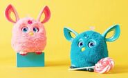 A Pink Furby Connect on a blue stand and Teal Furby Connect with lollipop