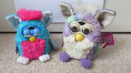 A Clown furby baby next to a Tye dye Furby.