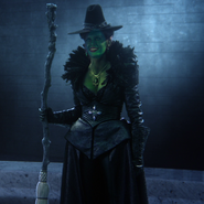 Zelena with green skin, black clothes and black pointy hat, on her broomstick, "A Curious Thing"