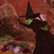 The Wicked Witch of the West with green skin, black clothes and black pointy hat, holding her broomstick, The Wizard of Oz