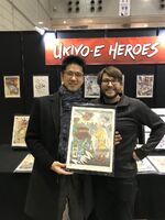 Murata tenant une planche fan-art à côté de l'illustrateur Jed Henry[1]