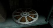 The image shows an old film reel for a projector, with light grey metal and yellowed film rolled up inside