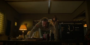 Joyce watching Hopper pushing a table back so they have enough room to connect the drawings.