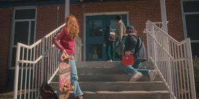 Lucas, Dustin, and Max watching Mike head inside the school building.