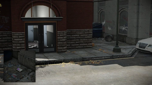 10. Between the blue garbage bin and the knocked down gray garbage bin, front of the fenced parking entrance