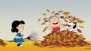 Linus and Snoopy playing with fallen leaves together as Lucy watches them