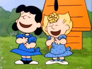 Lucy and Sally laughing behind Snoopy's doghouse