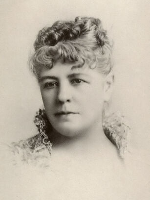 A fine charcoal portrait of Ina Coolbrith in her 30s or 40s, shown from the neck up, wearing a garment with a high, open collar made of lace, with hair curled and secured atop the head, looking slightly to the left. A fountain pen signature is below the portrait, reading "Ina Coolbrith", the letter "c" writ large to sweep underneath the next five letters.