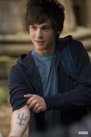 Logan Lerman incarnant Percy Jackson qui montre un tatouage inexistant dans les romans