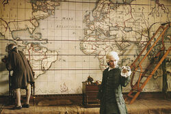 The artisan working on the world map while Cutler Beckett holds Norrington's sword as a pointer, talking to Weatherby Swann.