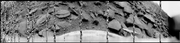 180-degree panorama of Venus's surface from the Soviet Venera 9 lander in 1975. Black-and-white image of barren, black, slate-like rocks against a flat sky. The ground and probe are the focus. Several lines are missing due to a simultaneous transmission of scientific data.