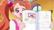 Ichika holds up the cookbook turned to the macaron recipe