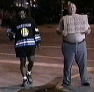 Norman Smiley and Ralphus stand outside with a "Will Wrestle For Food" sign.