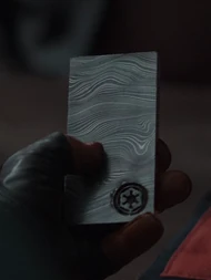 Din Djarin segura uma barra de beskar com o emblema imperial.