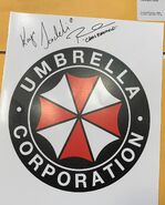 An Umbrella Corporation logo signed by Kaya Scodelario (Claire) and Robbie Amell (Chris)