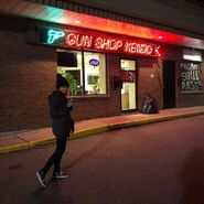 A fan takes photo in front of the shop, notice the herbs in the window, Maximum Standard ammo advertisement on the door, and the 'This Too Shall Pass!!!' graffiti from OG RE2.