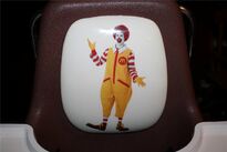 A toddler highchair featuring a picture of Ronald McDonald on the back rest cushion.