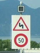 Panneau d'annonce d'un double virage accompagné d'une limitation de vitesse et d'un feu d'alerte clignotant. © Marcel Monterie