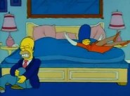 Marge jumps onto the bed, while Homer caresses his leg after hurting it.