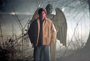 Clark stands in front of a statue angel, symbolizing his character