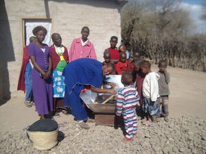 Naomi removing food from solar cooker to fireless cooker