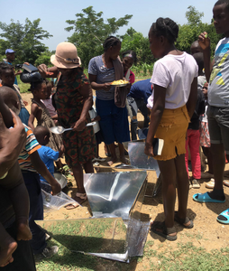 A crowd gathers around to inspect the solar cookers