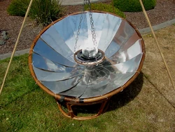 Close up of pot holding gimble made from small bike rim and coat hanger wire. Is baking cookies in a small pot on a black dish.