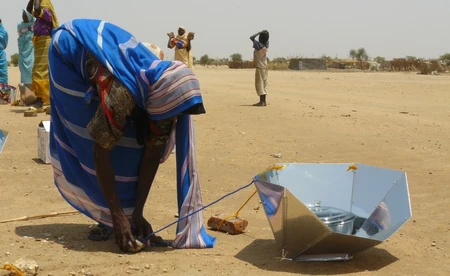 A Darfur refugee adjusts stones that secure a  solar cooker against the  in the  in 