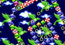 A psychodelic area, featuring a blue background with clouds and green birds. The foreground consists of a maze with rotating blocks. Sonic is continually spinning and making contact with colored blocks, which have a blue gemstone inside. Also visible are round tiles reading "up" or "R".
