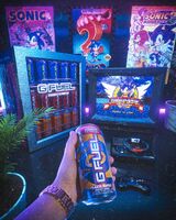 A promotional photo featuring a can of Peach Rings drink, a Sega Genesis that's playing Sonic 1, and 3 posters for Sonic games in the background